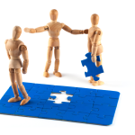 Jigsaw with one piece being held by a wooden doll