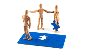 Jigsaw with one piece being held by a wooden doll