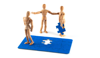 Jigsaw with one piece being held by a wooden doll